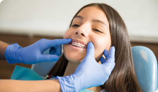 Dentist examining the metal braces of a young girl with a comfortable and smiling face