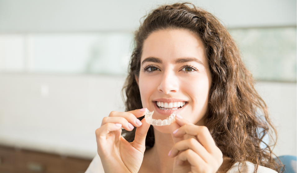 Smiling lady holding Invisalign aligner - Invisalign treatment by Living Water Dentistry, Surrey, BC