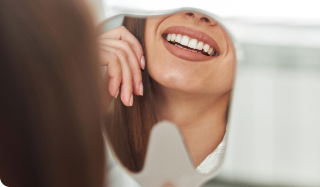 A Woman Who Has Undergone A Teeth Cleaning Treatment Looks Confidently In The Teeth-Shaped Mirror And Smiles |Teeth Cleaning Treatment In Surrey, BC.